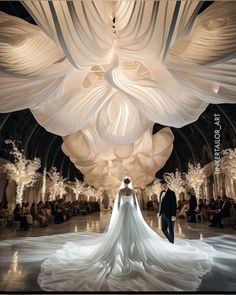 a bride and groom standing in front of an enormous white sculpture at the end of a hall