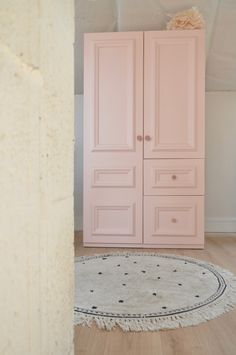 a room with a pink cabinet and rug on the floor in front of white walls