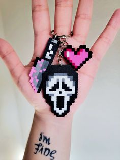 a hand holding two pixel keychains on it's thumb and one has a heart in the middle