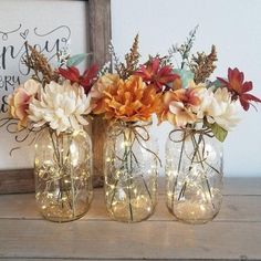 three mason jars filled with flowers and fairy lights on a table next to a framed sign