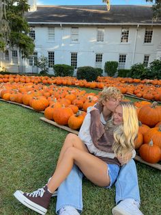 a woman sitting on the ground next to a man with long blonde hair in front of rows of pumpkins