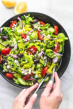 a salad with tomatoes, lettuce, onions and feta cheese in a black bowl