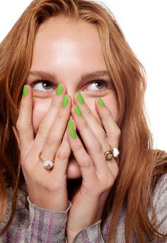 a woman covering her face with both hands and looking at the camera while wearing green nail polish