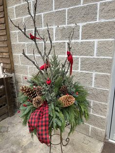 a potted plant with pine cones, evergreen and red cardinals on it sitting in front of a brick wall