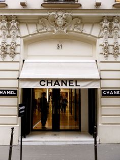 a chanel store front with people walking in the doorway and one person standing outside