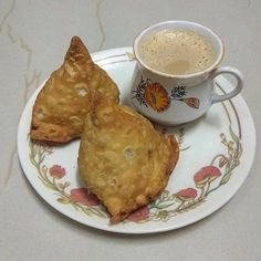 two pastries on a plate next to a cup of coffee and saucer with flower designs