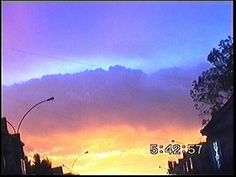 the sun is setting over some buildings and street lights in front of a cloudy sky