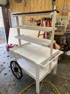 a white cart with wheels and shelves on it in a garage area next to other tools