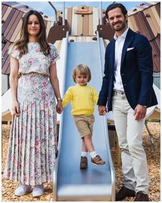 a man and woman holding hands while standing next to a child on a playground slide