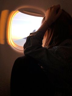 a woman sitting on an airplane looking out the window at the sunset or sunrise with her head in her hands