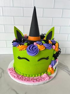 a green cake decorated with flowers and a unicorn's horn on top is sitting on a table