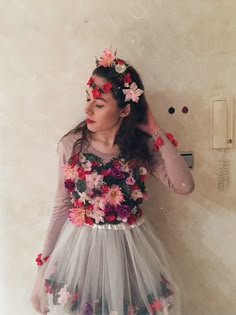 a woman with flowers in her hair standing next to a wall and holding her hands behind her head