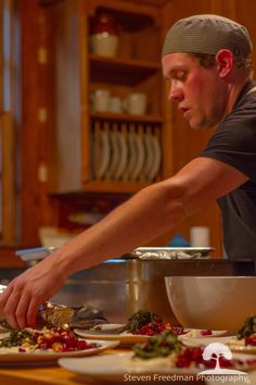 a man preparing food in a kitchen on top of a wooden table with plates and bowls