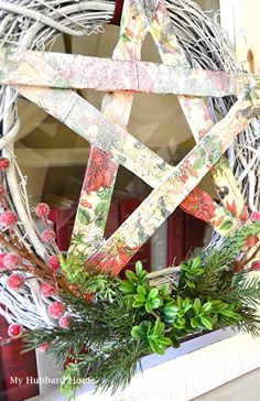 a christmas wreath with a star on it and greenery hanging from the front door