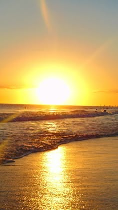 the sun is setting over the ocean with surfers