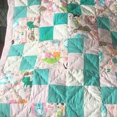 a baby quilt with animals on it is laying on a bed sheet that has pink and blue squares