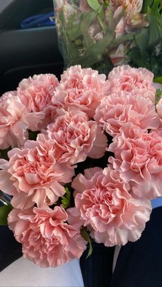 pink carnations are in a blue vase on the table next to other flowers