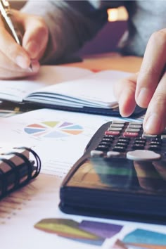 a person using a calculator on top of a desk with papers and pens