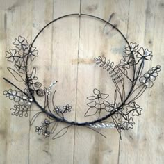 a wire wreath with flowers and leaves hanging on a wooden wall in the shape of a circle