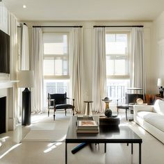 a living room filled with white furniture and windows covered in sheer draping next to a fire place