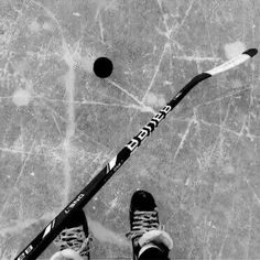 a person standing next to a hockey stick and ball on the ice in black and white