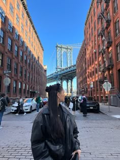 a woman is standing in the middle of an alleyway with buildings and a bridge behind her