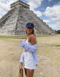 a woman is standing in front of an ancient pyramid wearing a hat and holding a straw bag