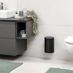 a black trash can sitting next to a white toilet in a bathroom with green rugs on the floor