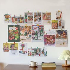 a wall covered in posters and pictures next to a table with a lamp on it