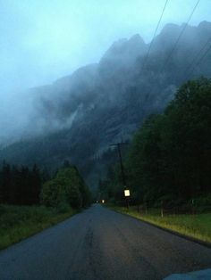 the clouds are rolling in over the mountains on a cloudy day at night, as cars drive down an empty road