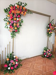 an arrangement of flowers and candles in front of a white wall with gold poles on the floor