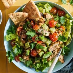 a salad with chicken, lettuce and tomatoes in a white bowl on a yellow table