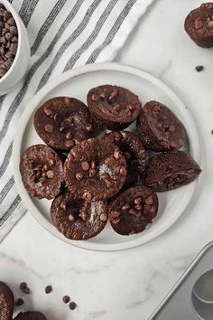 chocolate cookies on a white plate next to two bowls of chocolate chips and coffee beans