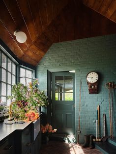 a kitchen with green brick walls and wooden ceiling, plants on the counter in front of the door