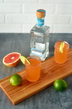 two glasses filled with grapefruit and lime on a cutting board next to a bottle of gin