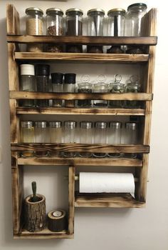 a wooden shelf filled with lots of jars and other items next to a wall mounted toilet paper dispenser