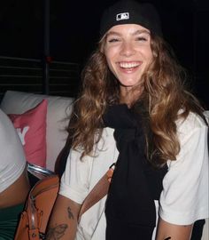 a woman with long hair wearing a black hat and white shirt smiling at the camera