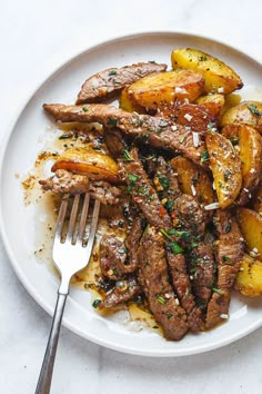 a white plate topped with steak and potatoes next to a fork on a marble table