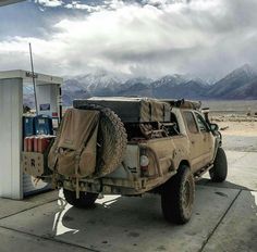 an army vehicle is parked at a gas station with mountains in the backgroud