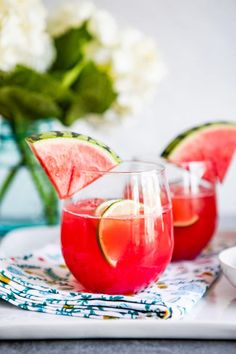 two glasses filled with watermelon and limeade sit on a tray next to flowers