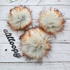 three furry pom poms sitting on top of a white wooden floor next to a pair of scissors