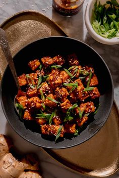 a bowl filled with tofu and green onions on top of a table next to sliced ginger