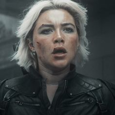 a woman with white hair and piercings in a black leather jacket looking at the camera