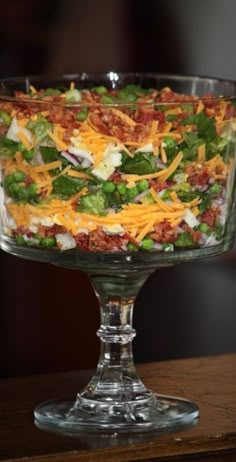 a salad in a glass bowl on top of a wooden table with cheese and other toppings