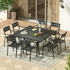 an outdoor dining table and chairs set up on a patio with potted plants in the background