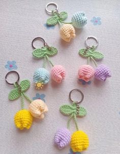 crocheted fruit keychains are arranged on a white tablecloth with blue flowers and green leaves