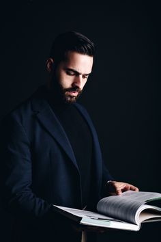 a man in a black jacket is holding a book and looking down at the pages