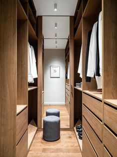 a walk - in closet with wooden cabinets and white shirts hanging on the walls, along with a stool