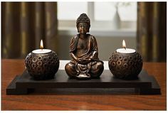 a buddha statue sitting on top of a wooden table next to two small candle holders