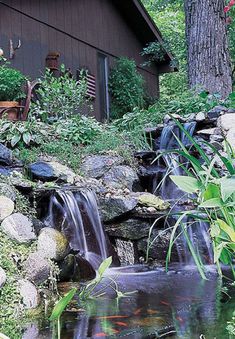 there is a small waterfall in the middle of some rocks and plants next to a building